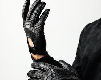 Könnte beinhalten: Ein Paar schwarze Lederhandschuhe mit Schlangenhautmuster. Die Handschuhe sind fingerlos und haben einen Knopfverschluss am Handgelenk.