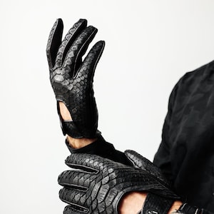 May include: A pair of black leather gloves with a snakeskin pattern. The gloves have a fingerless design and a button closure on the wrist.