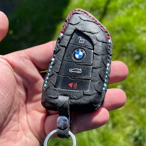 May include: Black leather key fob with a BMW logo and four buttons. The fob has a silver key ring attached.