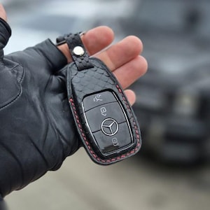 May include: A black leather key fob with red stitching and a silver key with four buttons. The key fob has a textured, snake-skin pattern.