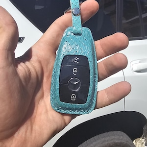 May include: A teal blue leather key fob with a black key inside. The key fob has a silver ring and a textured leather design.