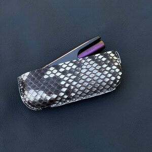 May include: A black and white snakeskin case with a purple and black electronic cigarette inside.