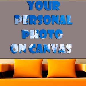 Puede incluir: Un lienzo gris con el texto "YOUR PERSONAL PHOTO ON CANVAS" en letras azules sobre un fondo de cielo y nubes. El lienzo est&aacute; colgado en una pared sobre un sof&aacute; naranja brillante.