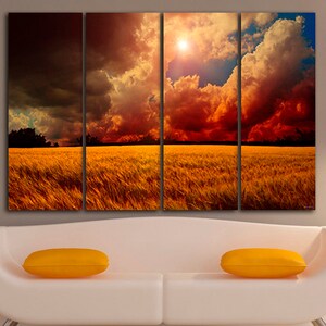 K&ouml;nnte beinhalten: Vierteiliges Leinwandbild, das einen dramatischen Sonnenuntergang &uuml;ber einem Weizenfeld zeigt. Der Himmel ist mit dunklen Wolken, feurigen Rott&ouml;nen und goldenem Sonnenlicht gef&uuml;llt. Das Feld hat eine warme goldene Farbe. Zwei gelbe Kissen liegen auf einem wei&szlig;en Sofa.