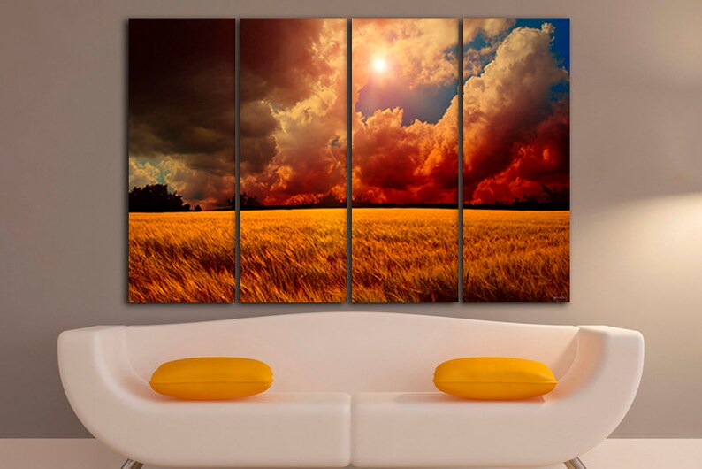 K&ouml;nnte beinhalten: Vierteiliges Leinwandbild, das einen dramatischen Sonnenuntergang &uuml;ber einem Weizenfeld zeigt. Der Himmel ist mit dunklen Wolken, feurigen Rott&ouml;nen und goldenem Sonnenlicht gef&uuml;llt. Das Feld hat eine warme goldene Farbe. Zwei gelbe Kissen liegen auf einem wei&szlig;en Sofa.