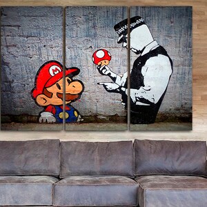 Pu&ograve; includere: Una stampa su tela a tre pannelli con un'illustrazione in bianco e nero di un poliziotto che tiene un fungo rosso e punta il dito verso un personaggio dei cartoni animati che assomiglia a Mario, che indossa un cappello rosso e una salopette blu.