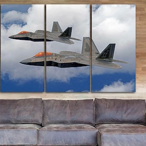 Könnte beinhalten: Zwei graue Kampfjets fliegen in Formation vor einem blauen Himmel mit weißen Wolken. Die Jets haben orangefarbene Akzente an der Nase und den Flügeln.