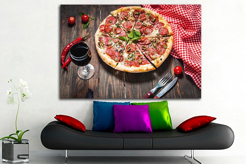 Puede incluir: Primer plano de una pizza de pepperoni con aceitunas verdes y albahaca sobre una mesa de madera con una copa de vino tinto, pimientos rojos y un mantel a cuadros rojo y blanco.