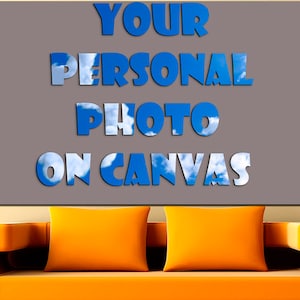 May include: A gray canvas with the text "YOUR PERSONAL PHOTO ON CANVAS" in blue letters with a sky and cloud background. The canvas is hanging on a wall above a bright orange couch.