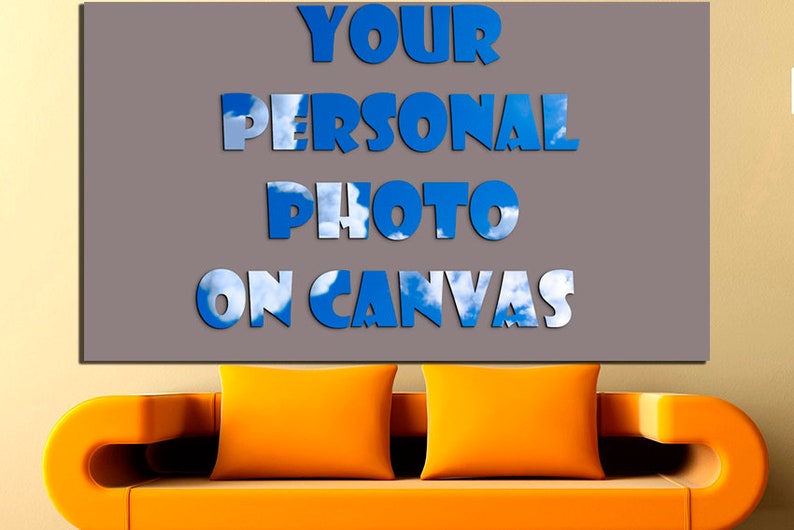 May include: A gray canvas with the text "YOUR PERSONAL PHOTO ON CANVAS" in blue letters with a sky and cloud background. The canvas is hanging on a wall above a bright orange couch.