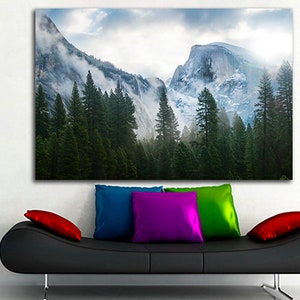 May include: A panoramic photograph of a mountain range with snow-capped peaks and a forest of evergreen trees in the foreground. The sky is cloudy and there is a hint of sunlight breaking through the clouds.