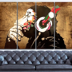 Op de afbeelding: Een meerdelige canvasprint met een gestileerde illustratie van een aap met een koptelefoon. Het gezicht van de aap is bedekt met kleurrijke verfspatten, en de achtergrond is een getextureerd bruin.