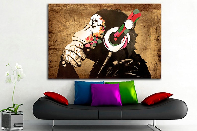 Op de afbeelding: Een kleurrijk abstract schilderij van een aap met een koptelefoon. De aap is afgebeeld in een zwart-wit silhouet met kleurspatten op zijn gezicht en koptelefoon. De achtergrond is een bruin, getextureerd canvas.