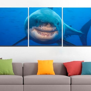 May include: A three-panel canvas print featuring a close-up of a great white shark with its mouth open, showing its teeth. The shark is swimming in blue water.