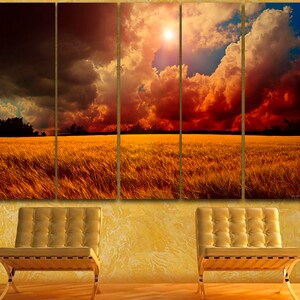 K&ouml;nnte beinhalten: Ein f&uuml;nfteiliger Leinwanddruck, der eine dramatische Landschaft zeigt. Das Kunstwerk zeigt ein goldenes Weizenfeld unter einem feurigen Himmel mit dunklen Wolken und einer hellen Sonne. Zwei goldfarbene St&uuml;hle stehen vor einer strukturierten gelben Wand.