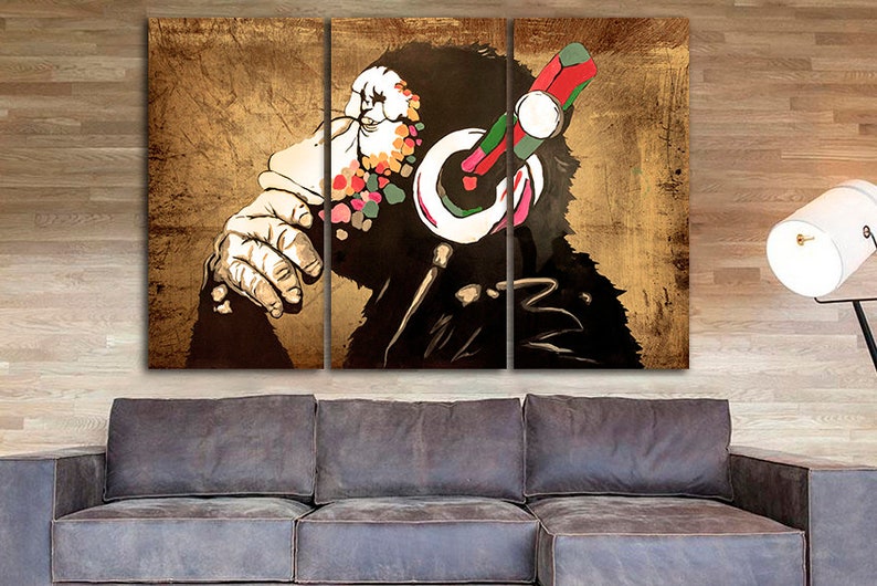 Op de afbeelding: Een driedelig canvasprint met een gestileerde afbeelding van een aap die een koptelefoon draagt met kleurrijke accenten. De achtergrond is van een textuur in goudkleur.