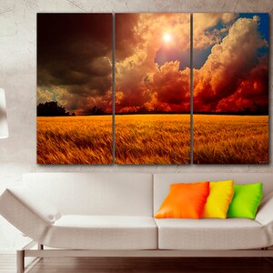 K&ouml;nnte beinhalten: Ein dreiteiliger Leinwanddruck, der eine dramatische Landschaft zeigt. Das Kunstwerk zeigt ein goldenes Feld unter einem feurigen Himmel mit dunklen, bedrohlichen Wolken. Die Sonne scheint hell und erzeugt einen Kontrast von Licht und Schatten. Die Szene weckt Ehrfurcht.