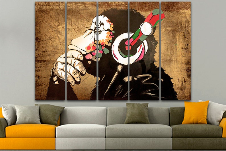 Op de afbeelding: Een meerdelige canvasprint met een gestileerde illustratie van een aap met een koptelefoon. Het gezicht van de aap is bedekt met kleurrijke verfspatten, en de koptelefoon is rood, groen en zwart. De achtergrond is een getextureerd bruin.