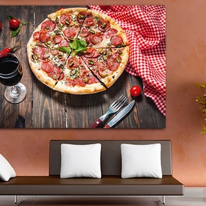 Puede incluir: Una pizza de pepperoni con aceitunas verdes y albahaca sobre una mesa de madera con un mantel a cuadros rojo y blanco, una copa de vino tinto y un tenedor y un cuchillo.