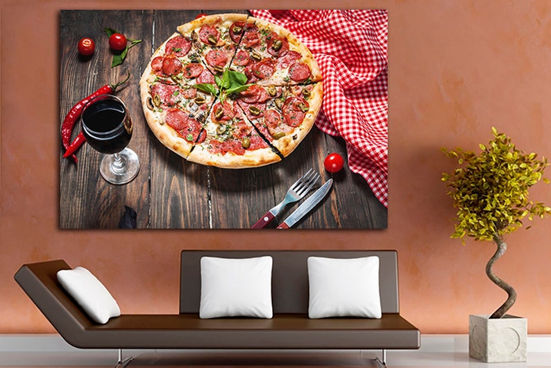 Puede incluir: Una pizza de pepperoni con aceitunas verdes y albahaca sobre una mesa de madera con un mantel a cuadros rojo y blanco, una copa de vino tinto y un tenedor y un cuchillo.