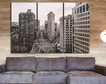 May include: A panoramic view of a city skyline with tall buildings, including the Flatiron Building, a distinctive triangular skyscraper. The buildings are made of brick and stone and have many windows. The street below is filled with people and traffic.