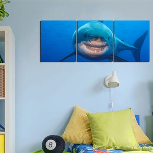 May include: A three-panel canvas print featuring a close-up of a great white shark with its mouth open, showing its teeth. The shark is swimming in blue water.
