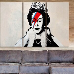 May include: A three-panel canvas print featuring a black and white portrait of Queen Elizabeth II with a red, blue, and white lightning bolt painted over her right eye. The queen is wearing a crown and a fur collar.