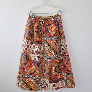 May include: A colorful, patterned skirt with a patchwork design. The skirt features a variety of geometric and floral patterns in shades of orange, red, blue, and white. It is hanging on a clear plastic hanger.