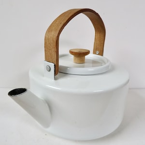 May include: White enamel tea kettle with a wooden handle and lid knob. The kettle has a curved spout and a simple, classic design. The handle is made of light-colored wood, and the lid knob is also wood. The kettle is a kitchenware item.