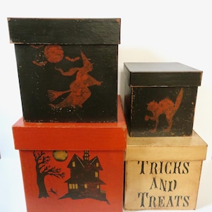 May include: A set of four square boxes with lids. Two black boxes feature orange silhouettes of a witch on a broomstick and a cat. One orange box displays a black haunted house and tree. One cream box features the black text TRICKS AND TREATS.