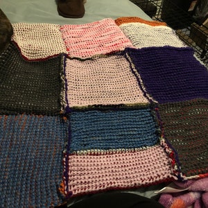 May include: A patchwork quilt with squares of different colors and textures, including pink, white, blue, purple, and gray.