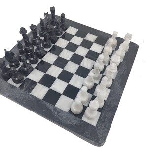 May include: A black and white marble chess set with black and white pieces on a black marble board.