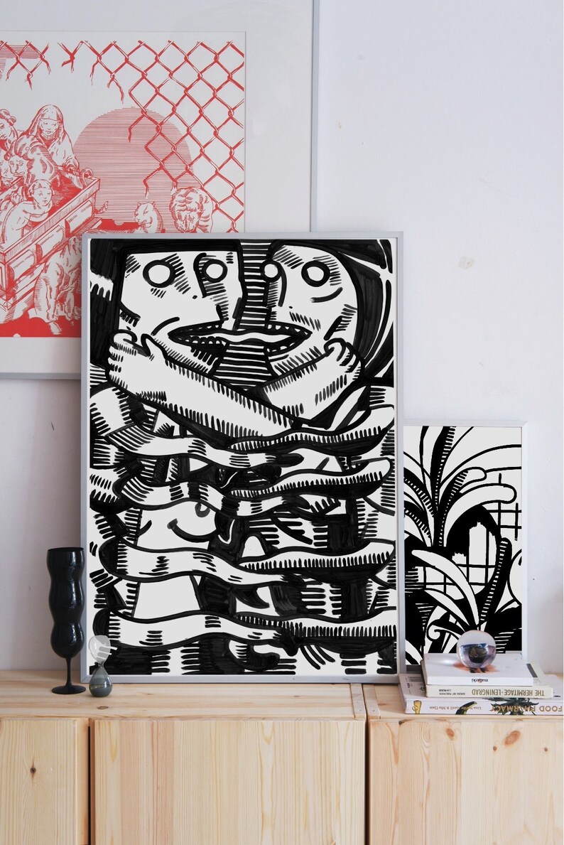 May include: Black and white illustration of two faces intertwined, creating a complex pattern of lines and shapes. The artwork is framed and displayed on a wooden shelf.