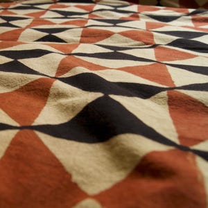 May include: A close-up of a fabric with a geometric pattern of black, white, and orange triangles. The fabric is textured and has a slightly wrinkled appearance.