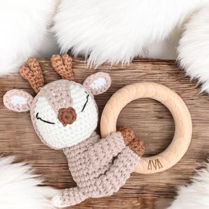 May include: A crocheted deer toy with a wooden teething ring. The ring is engraved with the name "AVA".