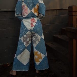 May include: A quilted two-piece set in a blue and white diamond pattern with accents of pink, yellow, and grey. The jacket has long sleeves and a collar, and the trousers are wide-legged.