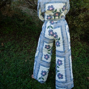 Può includere: Un completo trapuntato a due pezzi composto da una giacca a maniche lunghe e pantaloni a gamba larga. Il tessuto presenta uno sfondo color crema con un motivo a bordi a scacchi blu e bianchi e motivi floreali blu applicati con steli verdi.