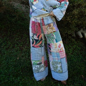 Può includere: Un completo trapuntato a due pezzi composto da una giacca a maniche lunghe con colletto e pantaloni a gamba larga. Il set è realizzato con vari quadrati di tessuto patchwork con motivi floreali, a quadri e botanici nei toni del blu, rosa e verde.