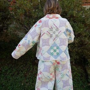 May include: A long-sleeve button-up jacket and matching wide-leg trousers made from a quilted fabric featuring a patchwork pattern of light purple, blue, green, and red geometric shapes on a cream-colored background with visible stitching.