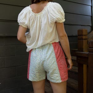 Puede incluir: Una blusa blanca con mangas cortas abullonadas. Los pantalones cortos presentan un diseño de patchwork, con un panel con estampado floral y un panel rojo con lunares blancos. Los pantalones cortos están hechos de una tela suave y ligera.