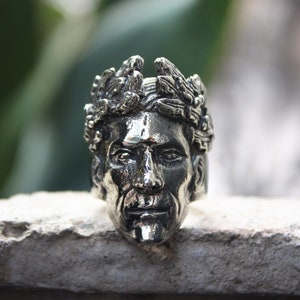 May include: A silver ring with a detailed sculpture of a face wearing a crown of leaves.