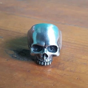 May include: A silver skull ring with a detailed design. The ring is made of metal and has a realistic skull design.