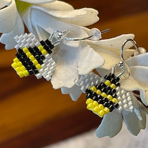 May include: A pair of silver hoop earrings with beaded bumblebees. The bees are black, yellow, and white.