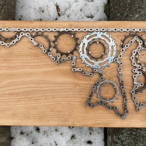 Puede incluir: Una placa de madera con el contorno del estado de Maryland creado usando una cadena de bicicleta y engranajes.