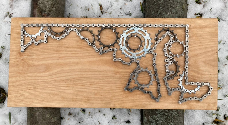 Puede incluir: Una placa de madera con el contorno del estado de Maryland creado usando una cadena de bicicleta y engranajes.