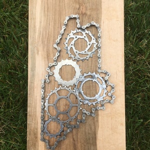 Puede incluir: Una placa de madera con un contorno met&aacute;lico del estado de Maine, creado con una cadena de bicicleta y engranajes.