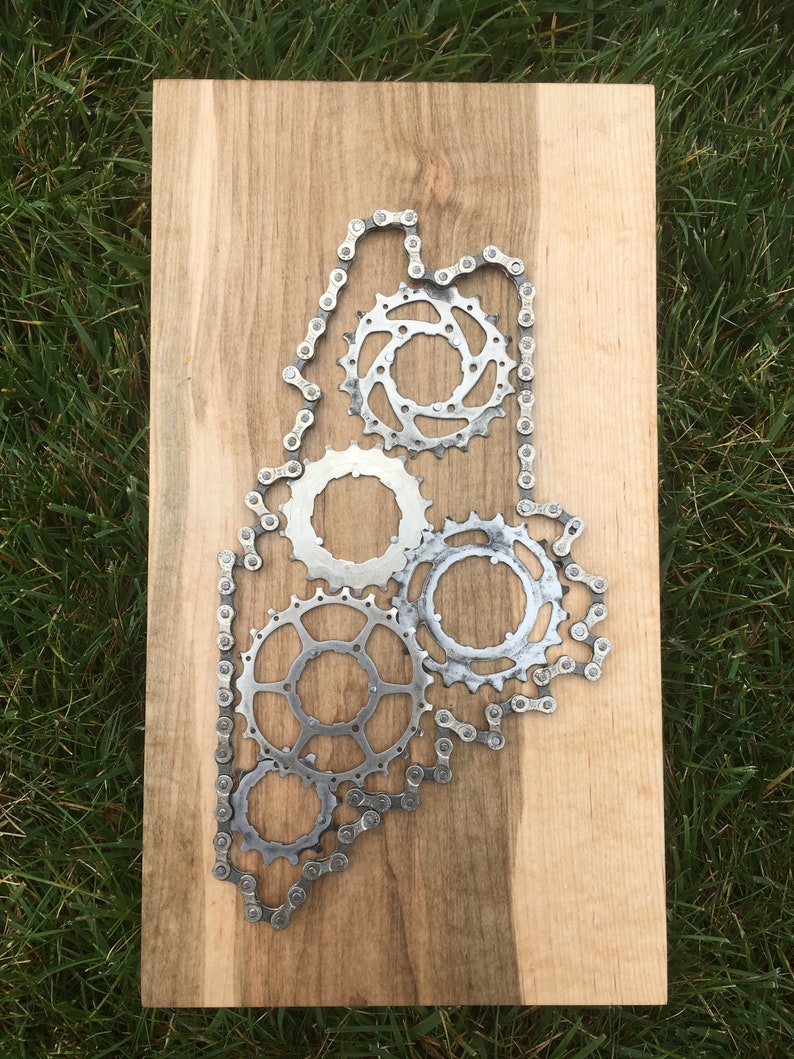 Puede incluir: Una placa de madera con un contorno met&aacute;lico del estado de Maine, creado con una cadena de bicicleta y engranajes.
