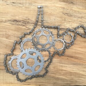 Puede incluir: Una pieza de arte met&aacute;lico con la forma del estado de Virginia Occidental, hecha de cadenas y engranajes de bicicleta. La pieza est&aacute; montada sobre un fondo de madera.