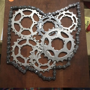 Puede incluir: Una pieza de arte met&aacute;lico con forma del estado de Ohio, hecha de cadena de bicicleta y engranajes. Los engranajes est&aacute;n dispuestos en un grupo en el centro del contorno del estado.