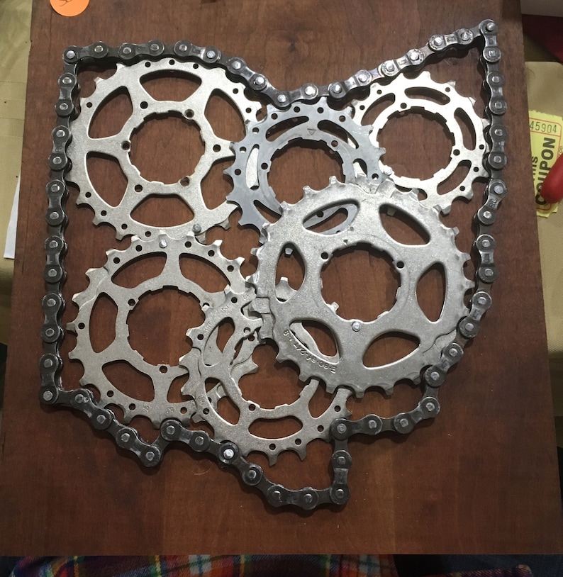 Puede incluir: Una pieza de arte met&aacute;lico con forma del estado de Ohio, hecha de cadena de bicicleta y engranajes. Los engranajes est&aacute;n dispuestos en un grupo en el centro del contorno del estado.